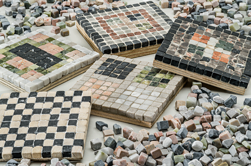 Fertige Mosaikbrettchen mit unterschiedlichen Mustern sowie dazwischen einzelen Steine in unterschiedlichen Farben. 